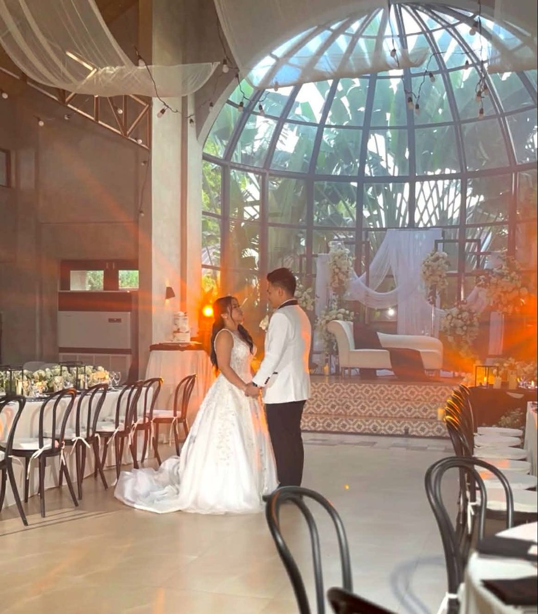A couple holding hands in a glass-domed atrium reception at golden hour, at a GO Events wedding.